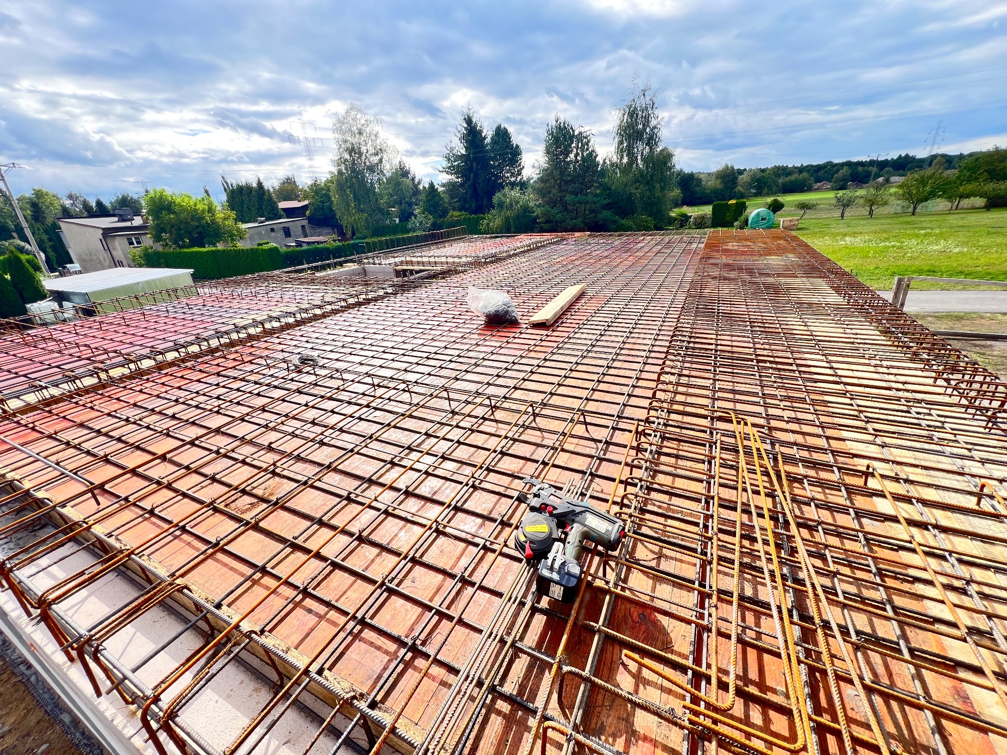 Zbrojenie stropu domu jednorodzinnego z użyciem wiązarki automatycznej. Widoczne pręty zbrojeniowe ułożone na szalunku, narzędzie do wiązania drutu i elementy mocujące.