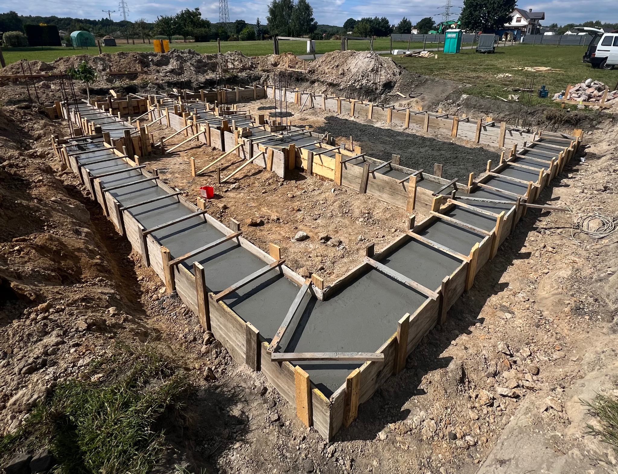 Zalane betonem szalunki fundamentów domu jednorodzinnego, widok z góry. Drewniane formy wypełnione świeżym betonem, przygotowane do dalszych prac budowlanych.