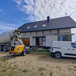 PREFBUD II DĄBROWSCY SPÓŁKA JAWNA - Betoniarka i agregat do wylewek na tle domu w trakcie budowy, błękitne niebo z obłokami w tle.