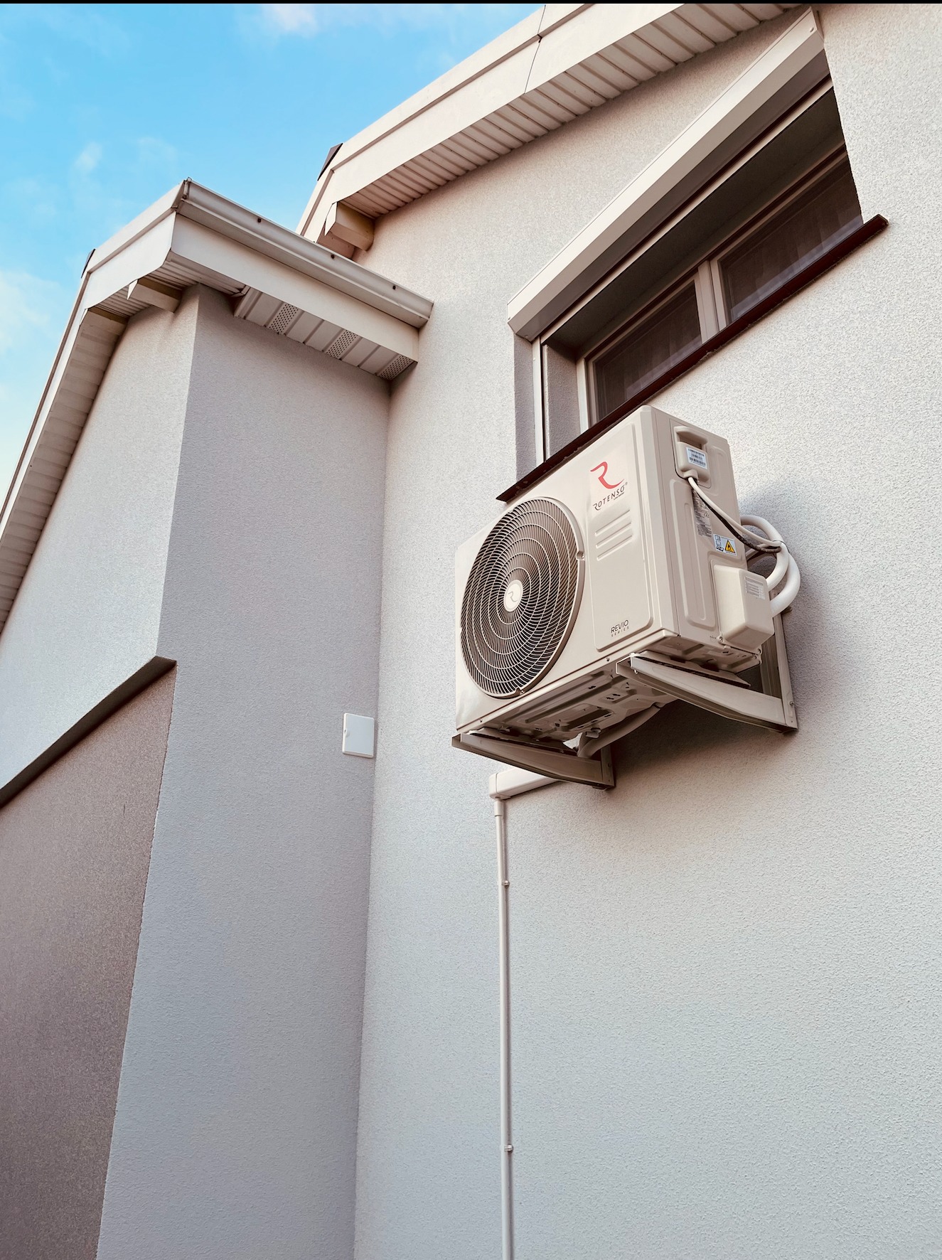 Zewnętrzna jednostka klimatyzacji Rotenso Revio zamontowana na elewacji budynku z widocznymi przewodami i wspornikami, ujęcie z dołu.