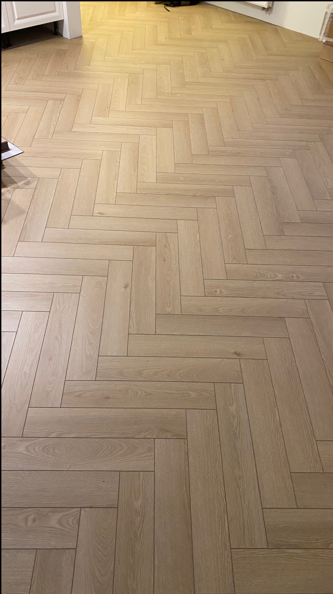 Jasne panele ułożone we wzór jodełki francuskiej na podłodze, widoczne fragmenty białych mebli w tle.