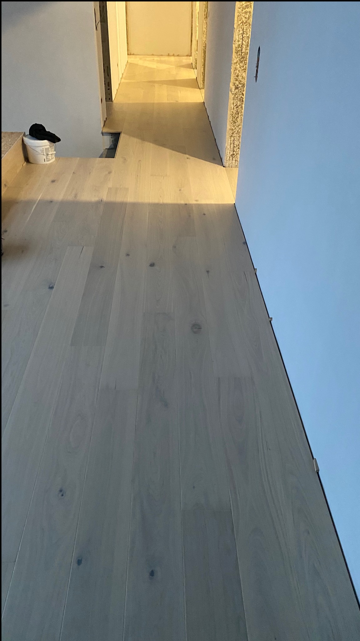 Jasne panele podłogowe ułożone w korytarzu w Gdańsku, widoczny kubeł z narzędziami malarskimi i niedokończone ściany.