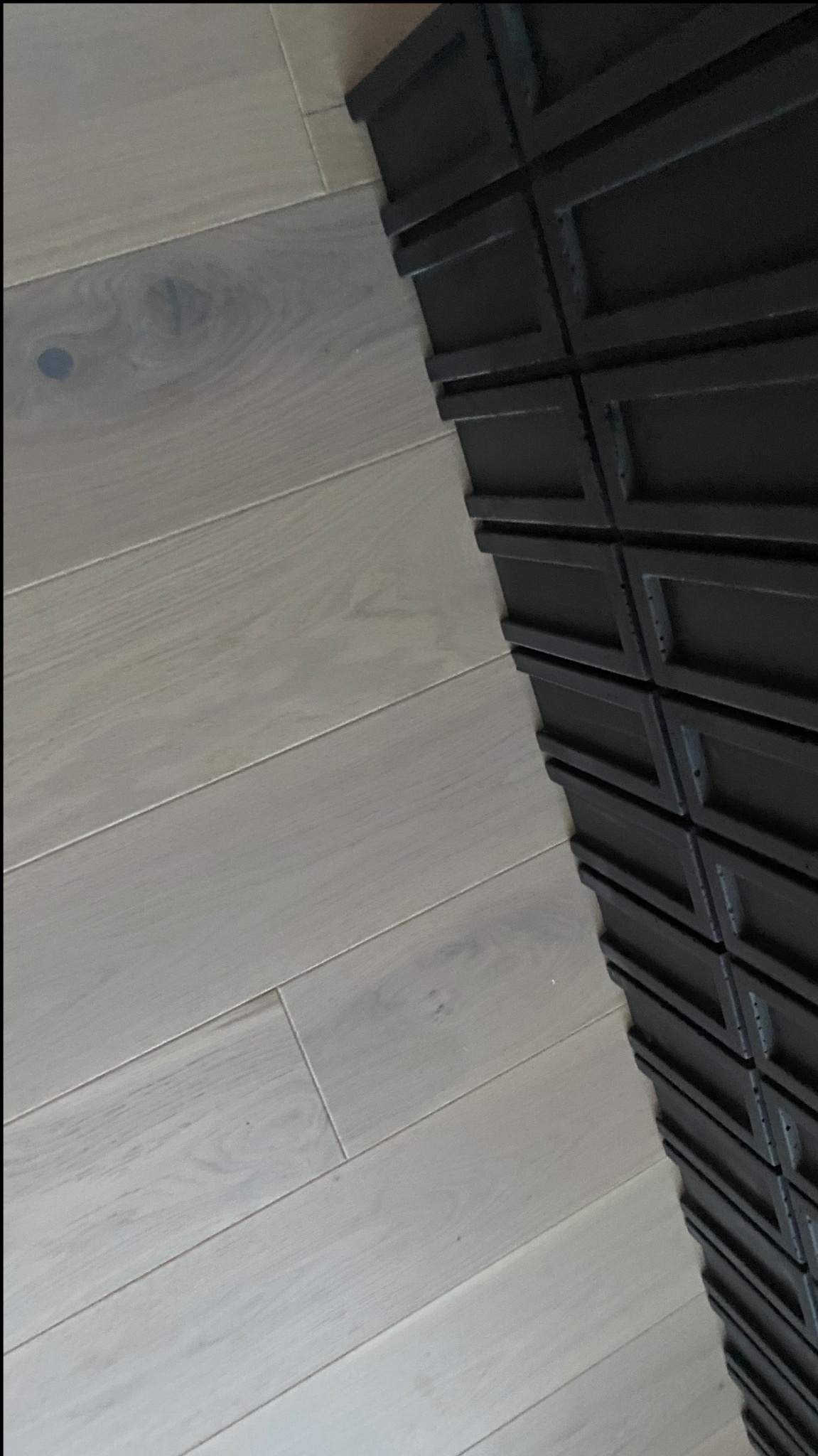 Jasne, szerokie deski parkietu ułożone ukośnie, sąsiadujące z ciemną, ozdobną listwą przypodłogową.