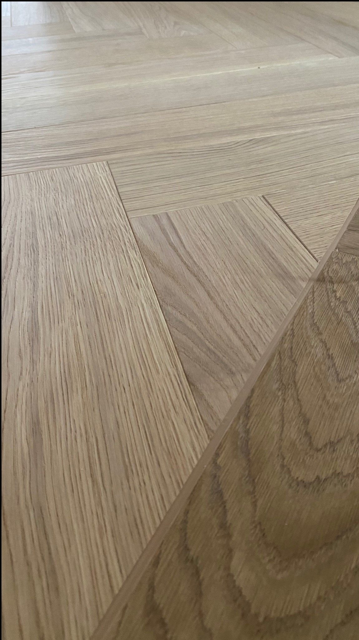 Jasny parkiet ułożony we wzór jodełki francuskiej, z widocznym zbliżeniem na łączenie klepek.