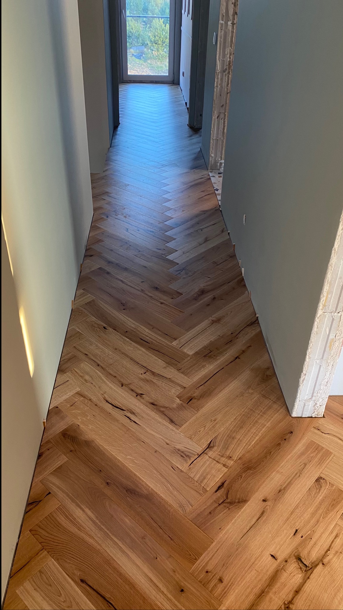 Ułożony parkiet w jodełkę francuską w korytarzu, widoczne niedokończone wykończenia ścian.