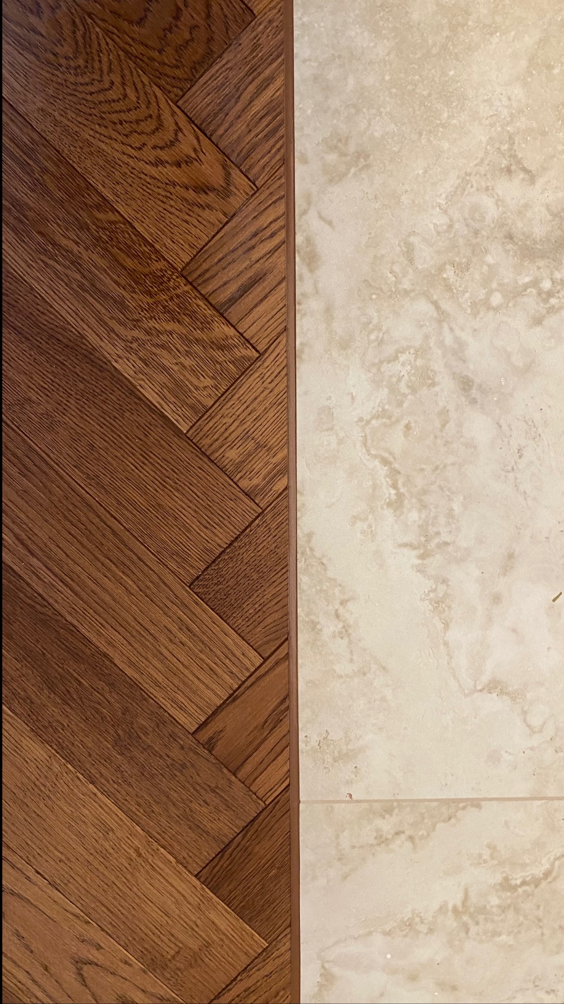 Połączenie parkietu ułożonego w jodełkę z beżowymi płytkami imitującymi marmur, widoczne z góry.