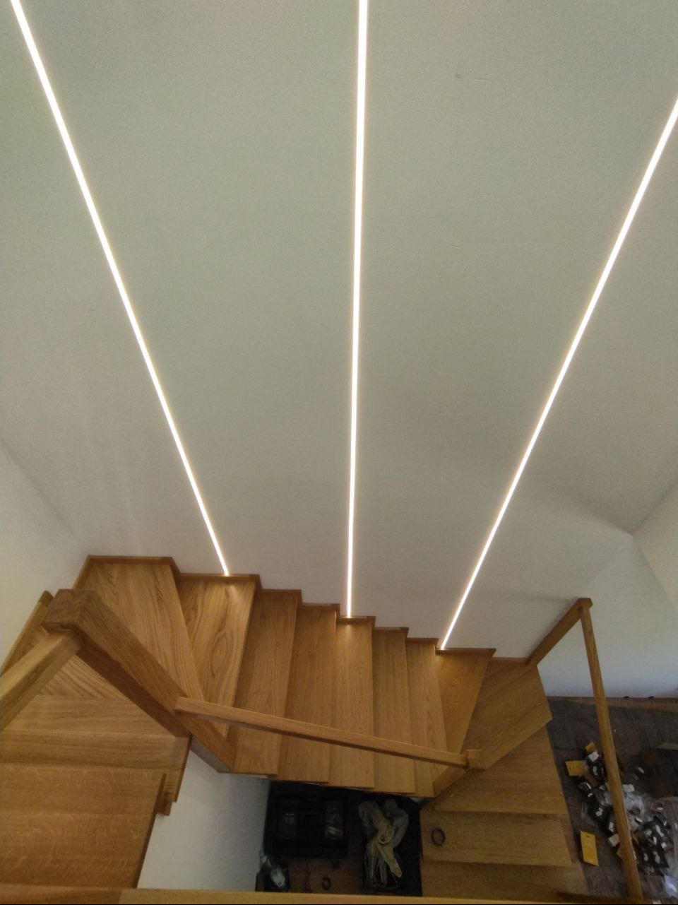 Oświetlenie LED liniowe w suficie nad drewnianymi schodami, widok z dołu, ciepłe światło.