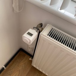 Zicher Technika Grzewcza Mateusz Dziembowski - Biały grzejnik z elektronicznym termostatem pokazującym temperaturę 22 stopni Celsjusza, zamontowany przy oknie z żaluzjami i drewnianej podłodze.