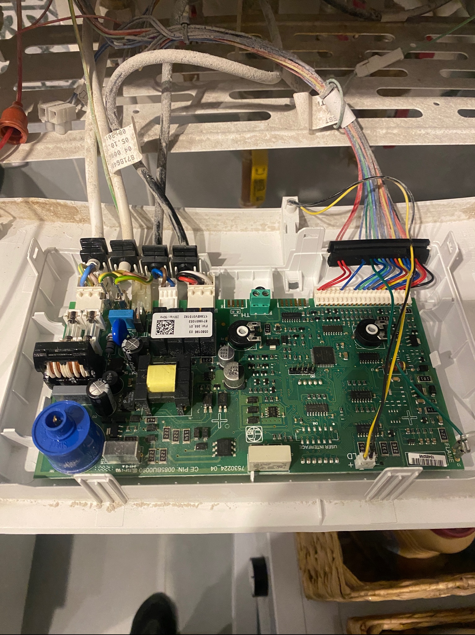 Otwarta obudowa pieca z widoczną, zakurzoną płytą sterującą, licznymi przewodami i elementami elektronicznymi. Widoczne etykiety i oznaczenia na płycie.