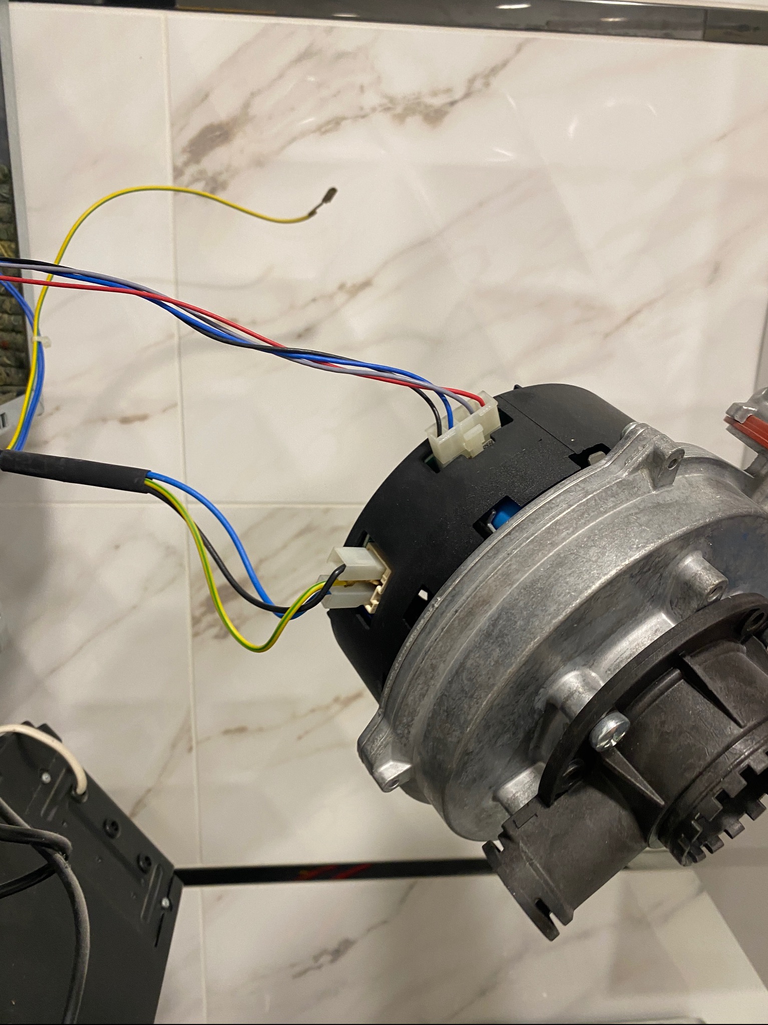 Metalowa obudowa z czarnym elementem i podłączonymi kolorowymi przewodami na tle marmurowej płytki.