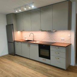 Paweł Nikiel - Nowoczesna kuchnia w odcieniach szarości z drewnianym blatem, oświetleniem punktowym i marmurowym backsplash, widziana z perspektywy podłogi z paneli.