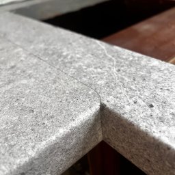 Paweł Nikiel - Szary, kamienny blat kuchenny z widocznym łączeniem narożnym, ukazujący precyzję wykonania i dopasowanie do zabudowy. Minimalistyczny design, surowy materiał.
