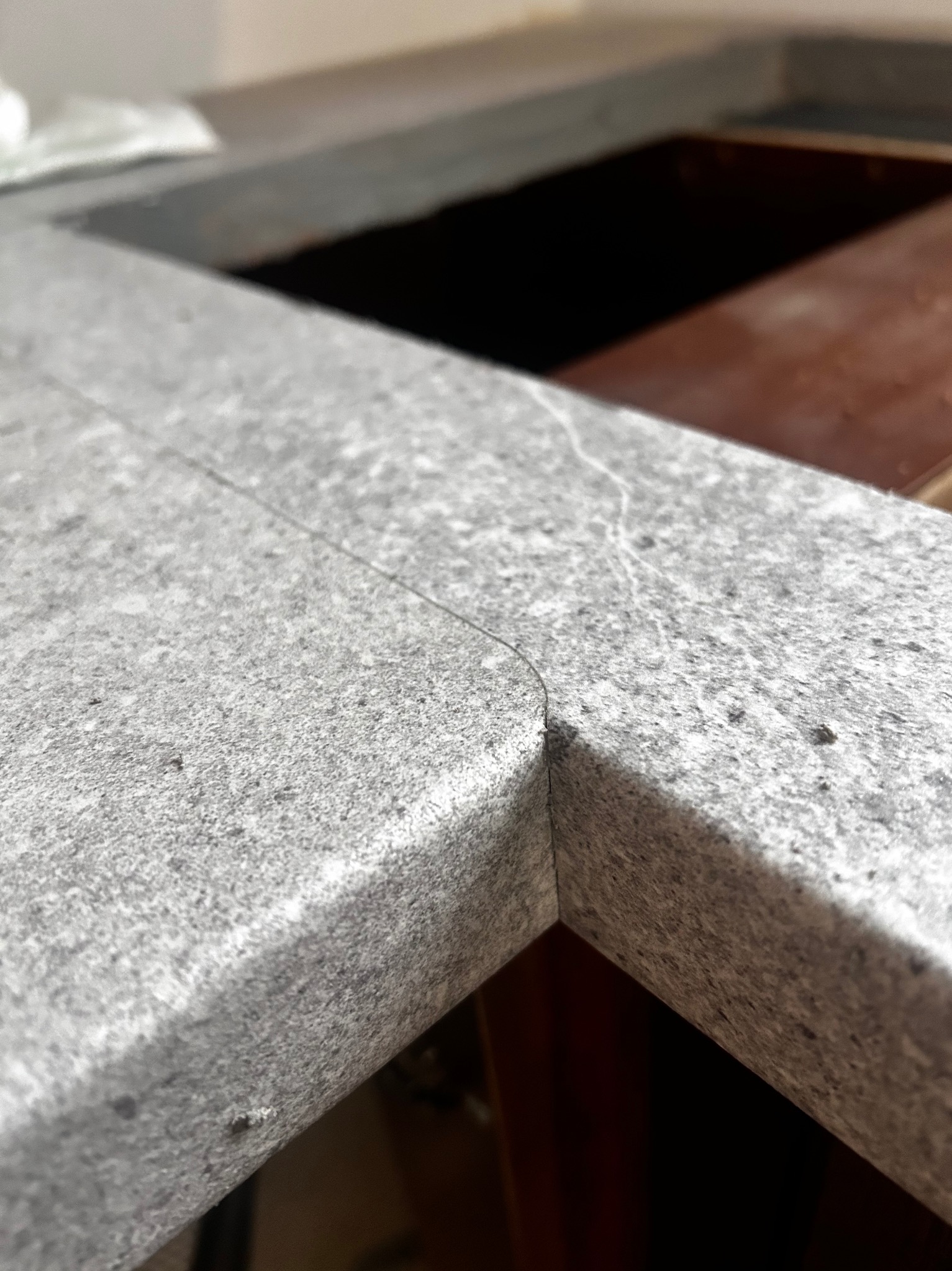 Szary, kamienny blat kuchenny z widocznym łączeniem narożnym, ukazujący precyzję wykonania i dopasowanie do zabudowy. Minimalistyczny design, surowy materiał.