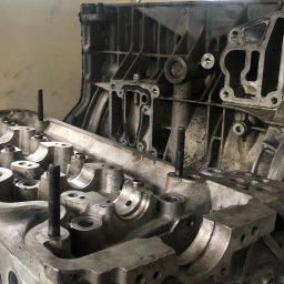 Mechanika Pojazdowa Serwis Chłodnic i Głowic Samochodowych - Zdemontowana aluminiowa głowica silnika samochodowego z wystającymi śrubami, widoczny blok silnika w tle.
