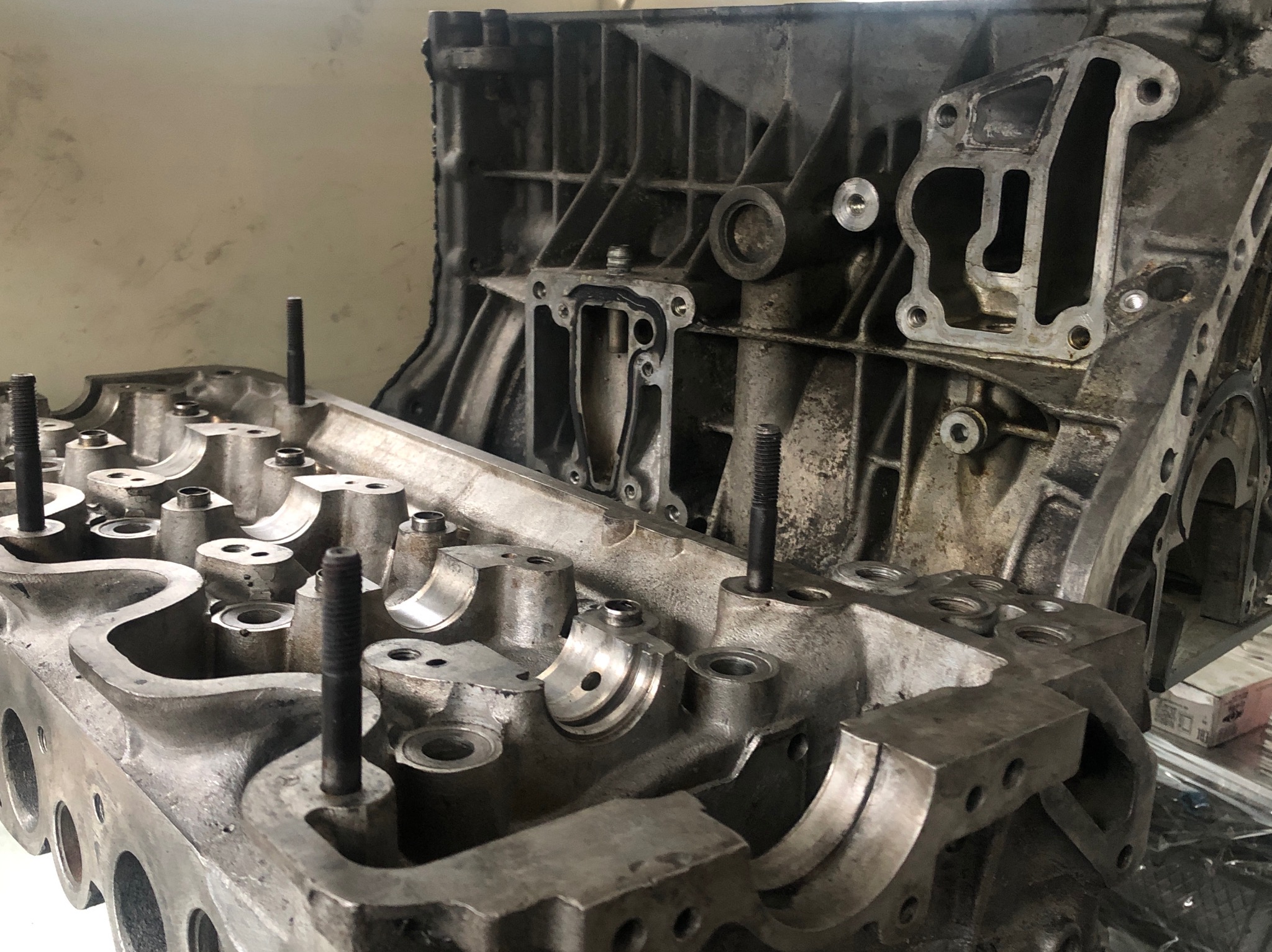 Zdemontowana aluminiowa głowica silnika samochodowego z wystającymi śrubami, widoczny blok silnika w tle.