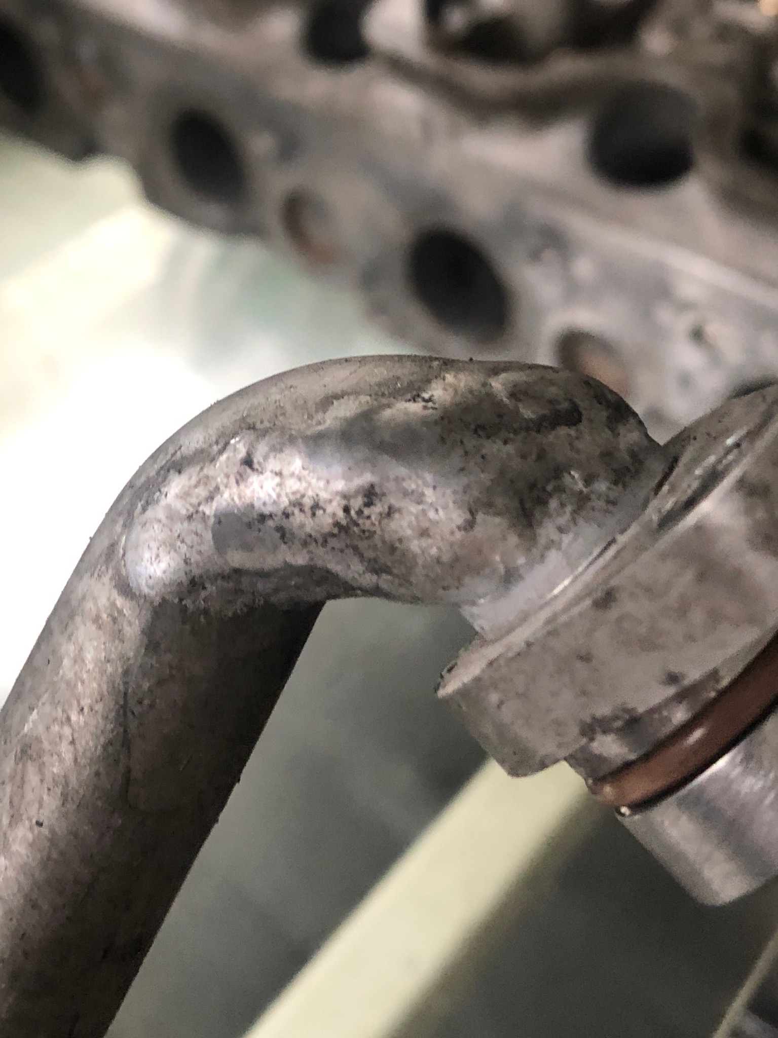 Detail of a corroded metal pipe connected to an engine block, showing signs of wear and tear.