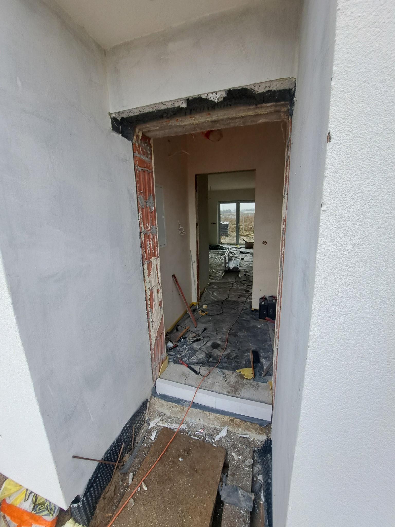 Przygotowanie do montażu ościeżnicy w surowym wnętrzu, widoczne narzędzia i materiały budowlane, ściany w trakcie wykańczania.