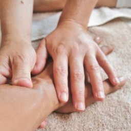 Przychodnia MOJA Ochota Warszawa - Fizjoterapia i Rehabilitacja - Dłonie terapeuty uciskają dłoń pacjenta na beżowym ręczniku podczas zabiegu manualnego.