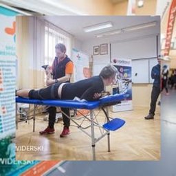 Przychodnia MOJA Ochota Warszawa - Fizjoterapia i Rehabilitacja - Pacjent leżący na stole do masażu w Warszawie, podczas zabiegu manualnego wykonywanego przez terapeutę. Widoczne logo firmy na ścianie w tle.