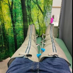 Przychodnia MOJA Ochota Warszawa - Fizjoterapia i Rehabilitacja - Pacjent w spodniach do presoterapii leżący na leżance, tło z motywem lasu w gabinecie.