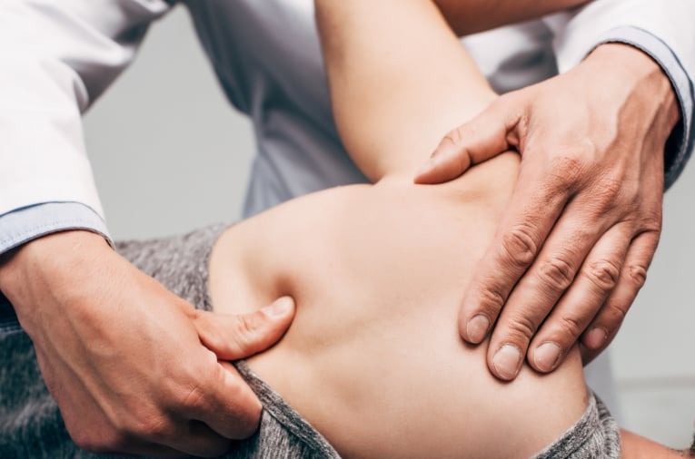Rehabilitant w białym uniformie uciska kciukiem punkt spustowy na plecach pacjenta leżącego na brzuchu, widoczne napięcie mięśni