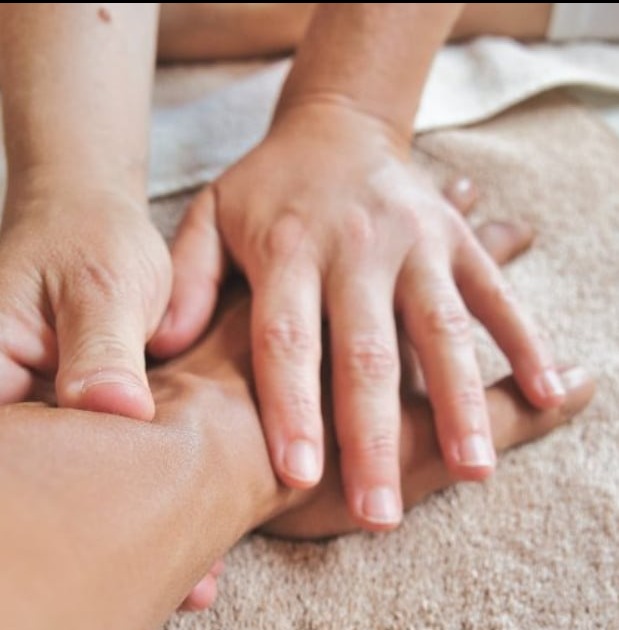 Dłonie terapeuty uciskają dłoń pacjenta na beżowym ręczniku podczas zabiegu manualnego.