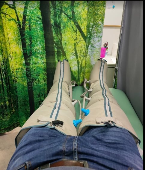 Pacjent w spodniach do presoterapii leżący na leżance, tło z motywem lasu w gabinecie.