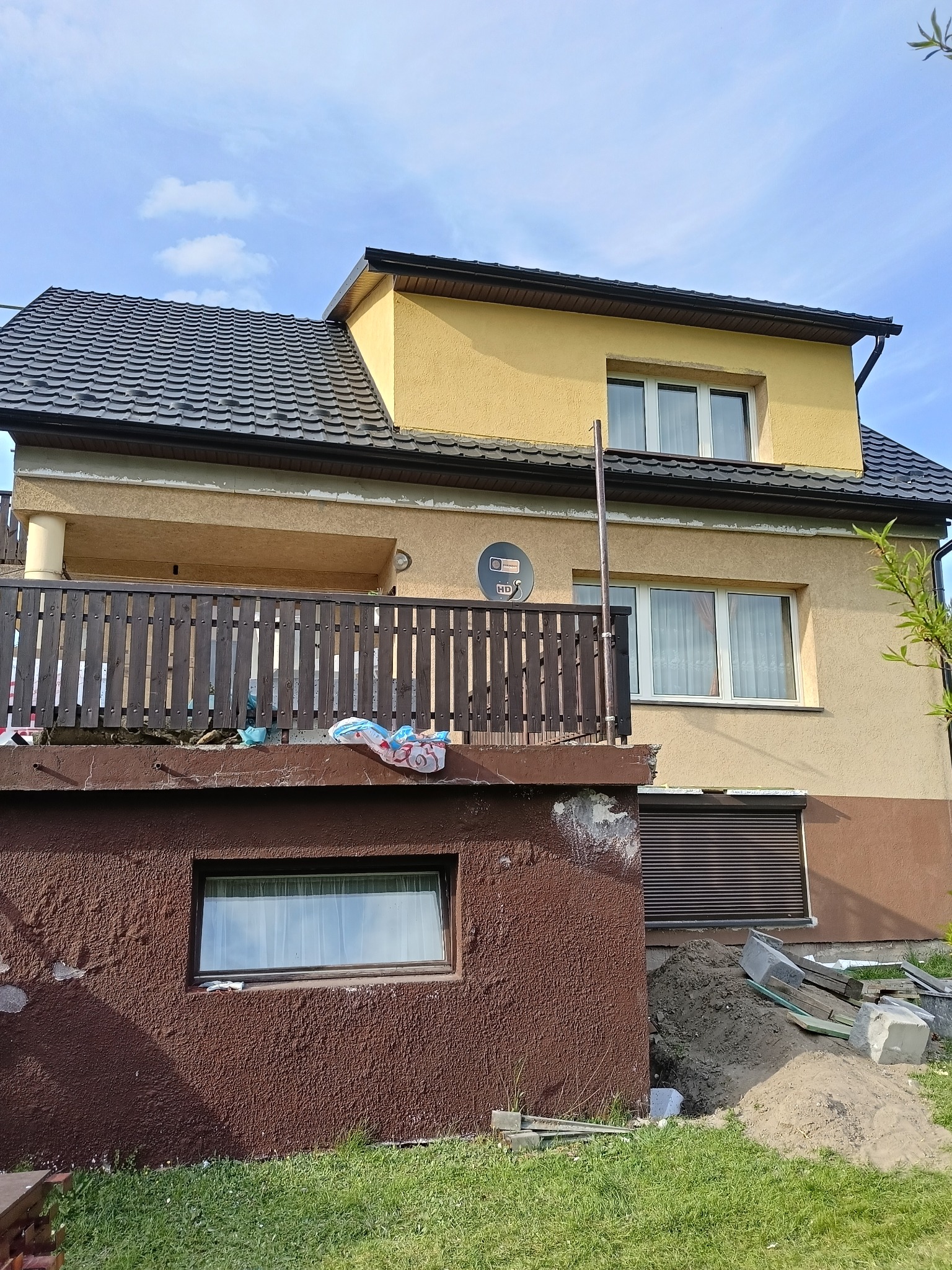 Dwukondygnacyjny dom z balkonem przed remontem elewacji. Widoczne uszkodzenia tynku i przygotowane materiały budowlane. Ujęcie w słoneczny dzień.