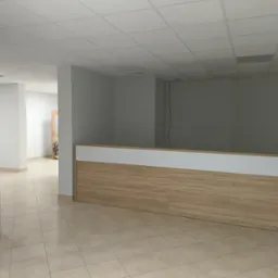 Nowe biuro: jasne płytki podłogowe, białe ściany i sufit kasetonowy, drewniana lada recepcyjna z białym blatem, widok z korytarza.