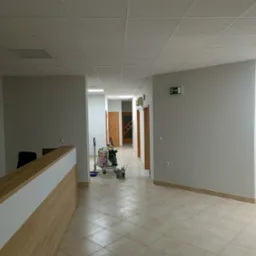 Korytarz biurowy z recepcją, świeżo po malowaniu ścian na jasny odcień szarości, w tle wózek z narzędziami malarskimi i wiaderkiem farby.