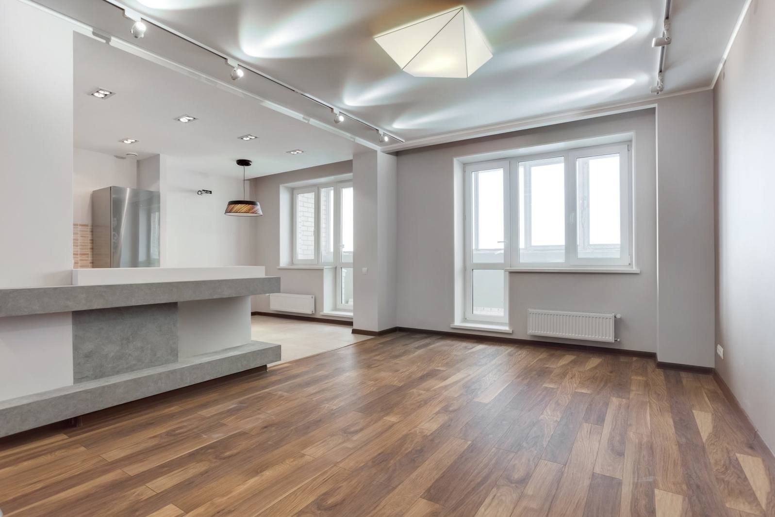 Jasne, przestronne wnętrze po remoncie z drewnianą podłogą, białymi ścianami i oknami, oraz nowoczesnym oświetleniem sufitowym.