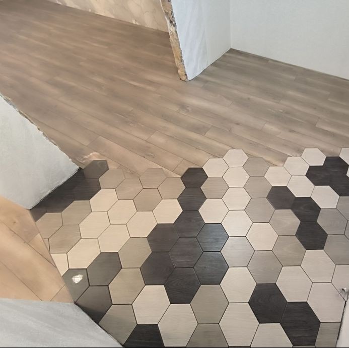 Połączenie podłogi drewnopodobnej i heksagonalnych płytek w odcieniach szarości, beżu i czerni, widoczne niedokończone wykończenie ściany.