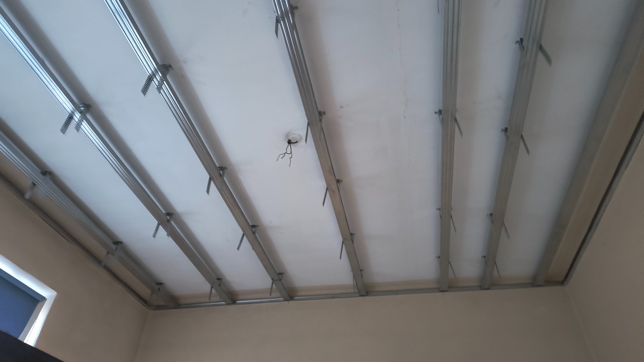 Montaż sufitu podwieszanego z płyt kartonowo-gipsowych na metalowej konstrukcji, widoczne profile i zawiesia, fragment instalacji elektrycznej