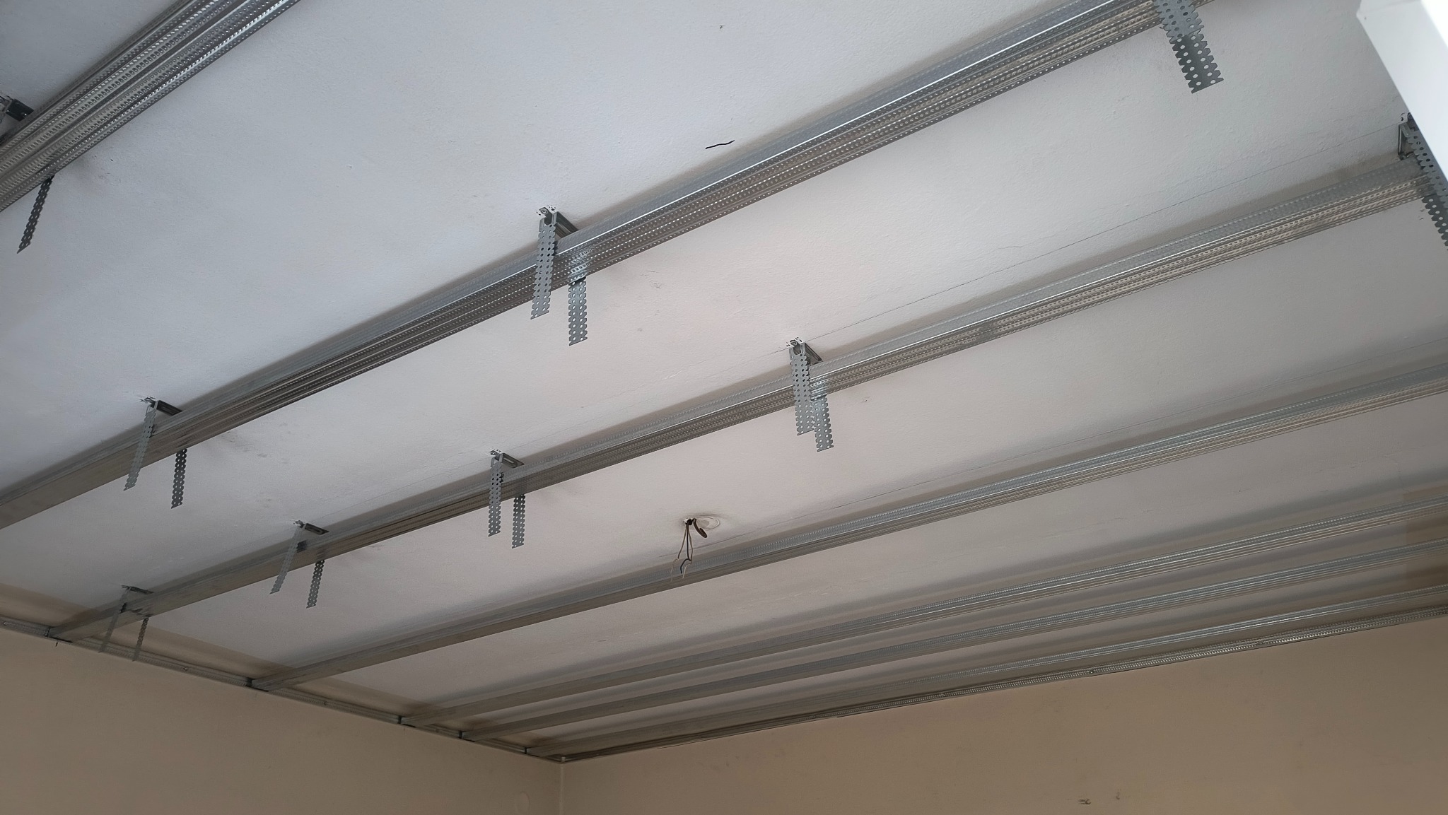 Sufit z widoczną metalową konstrukcją podwieszaną, przygotowaną do montażu płyt kartonowo-gipsowych, z widocznymi profilami i wieszakami.