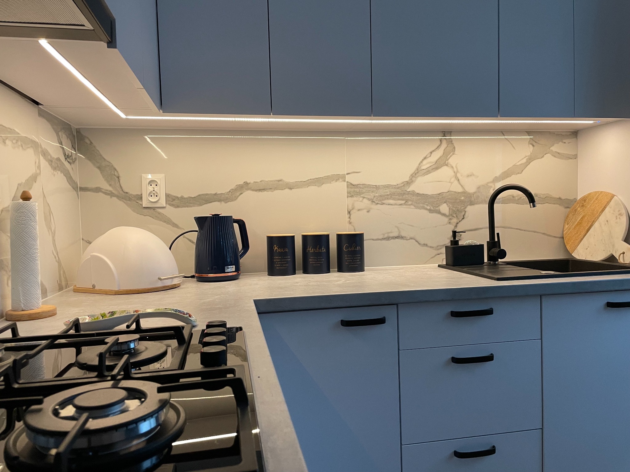 Nowoczesna kuchnia w Tokarni z szarymi szafkami, marmurowym backsplash'em, czarną armaturą i oświetleniem LED pod szafkami.