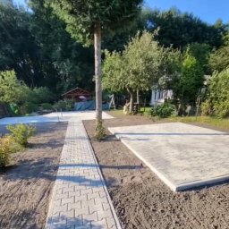 Brukisiema Mateusz Szczepaniak - Ścieżka i plac z jasnoszarej kostki brukowej w ogrodzie, widok na altanę i zieleń w tle, świeżo ułożona kostka, częściowo przygotowany teren.