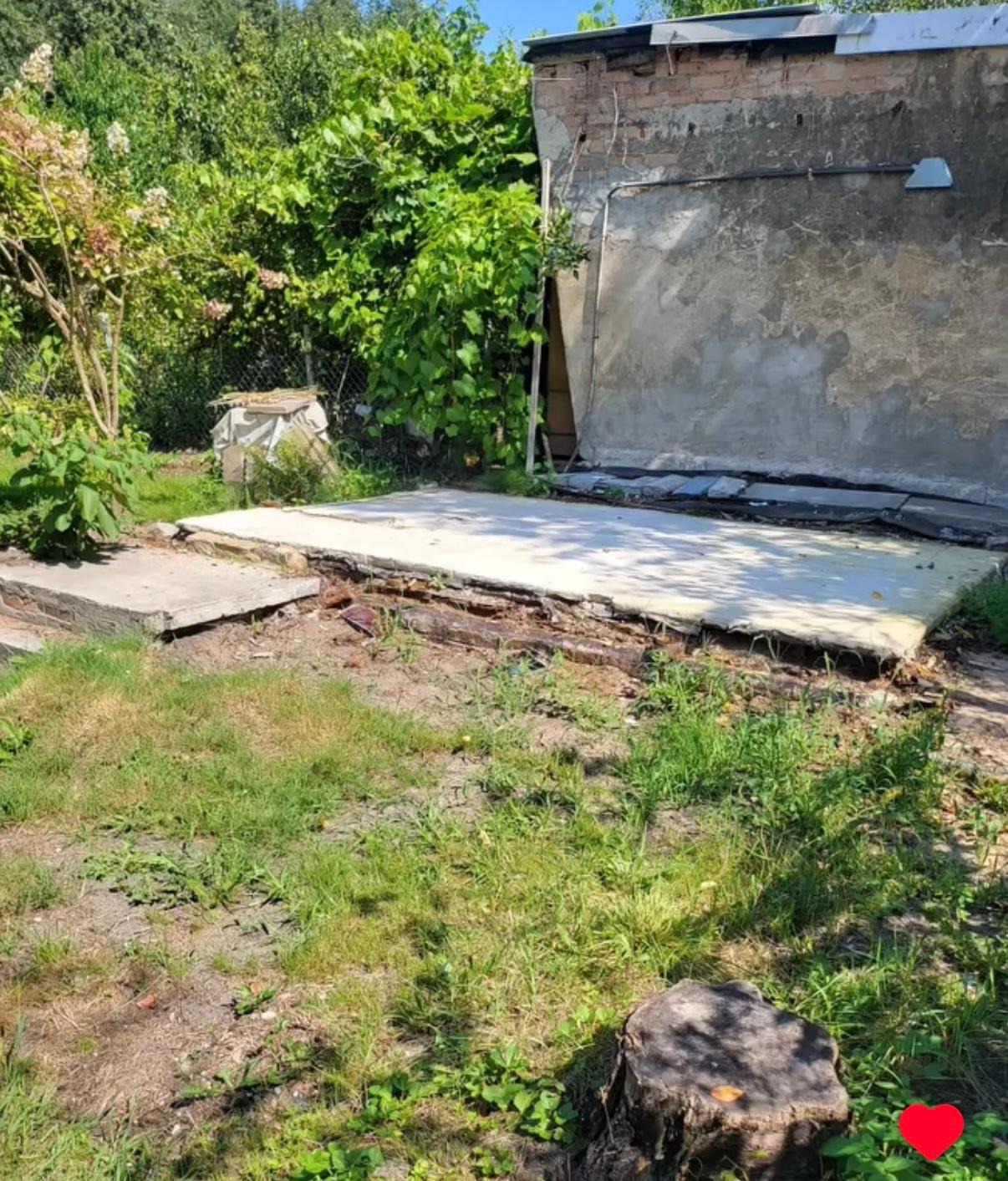 Przygotowany teren pod wylewkę, widoczne resztki starej konstrukcji, zarośnięty trawnik i fragment ściany budynku w tle. Prace ziemne przed wylaniem fundamentów.