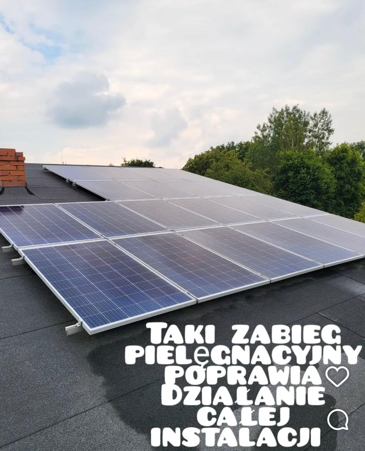 Panele słoneczne na dachu pokrytym papą, widoczne z dołu pod kątem. W tle zieleń drzew i pochmurne niebo. Na zdjęciu tekst informujący o zabiegu pielęgnacyjnym.