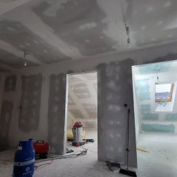 MBIT - Wnętrze w trakcie prac wykończeniowych: ściany i sufit pokryte płytami, widoczne szpachlowanie, butla gazowa, odkurzacz przemysłowy i narzędzia.
