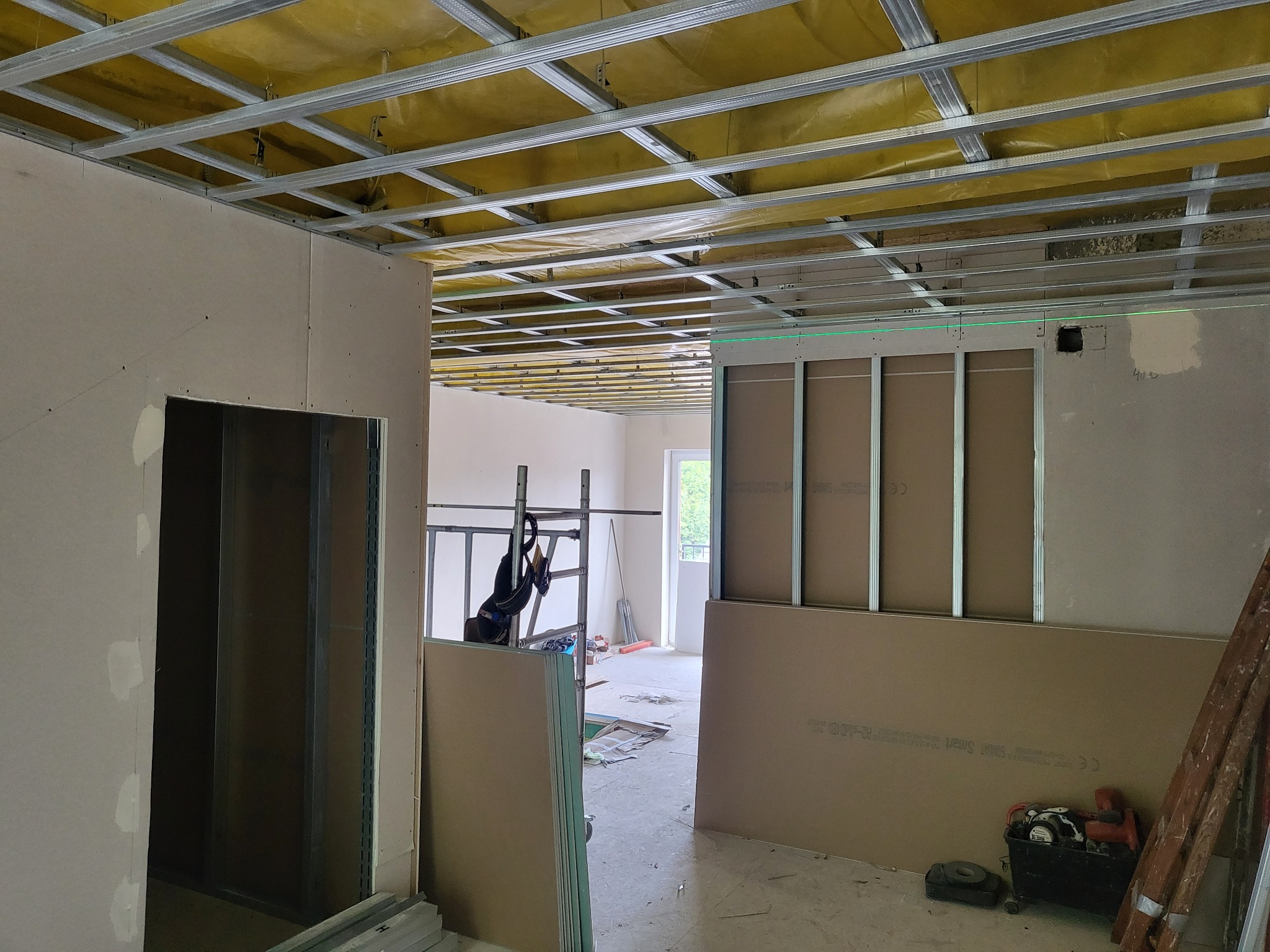 Wnętrze w trakcie montażu płyt karton-gips na ścianach i suficie, widoczne metalowe profile, ocieplenie sufitu wełną mineralną i narzędzia pracy.