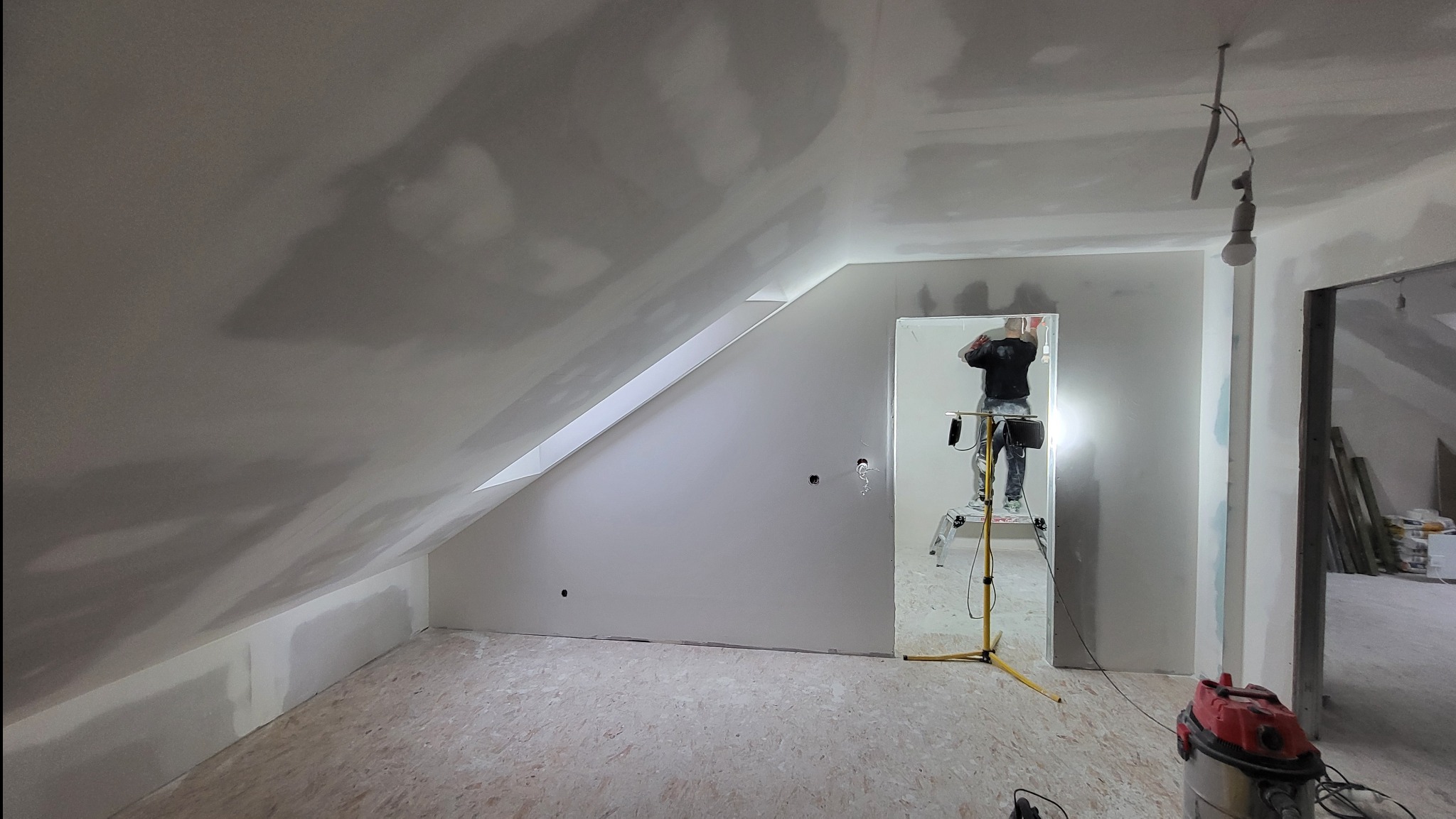 Poddasze po montażu płyt, widoczny pracownik na drabinie szpachlujący łączenia, niedokończone wykończenie, na podłodze płyty OSB i odkurzacz przemysłowy.