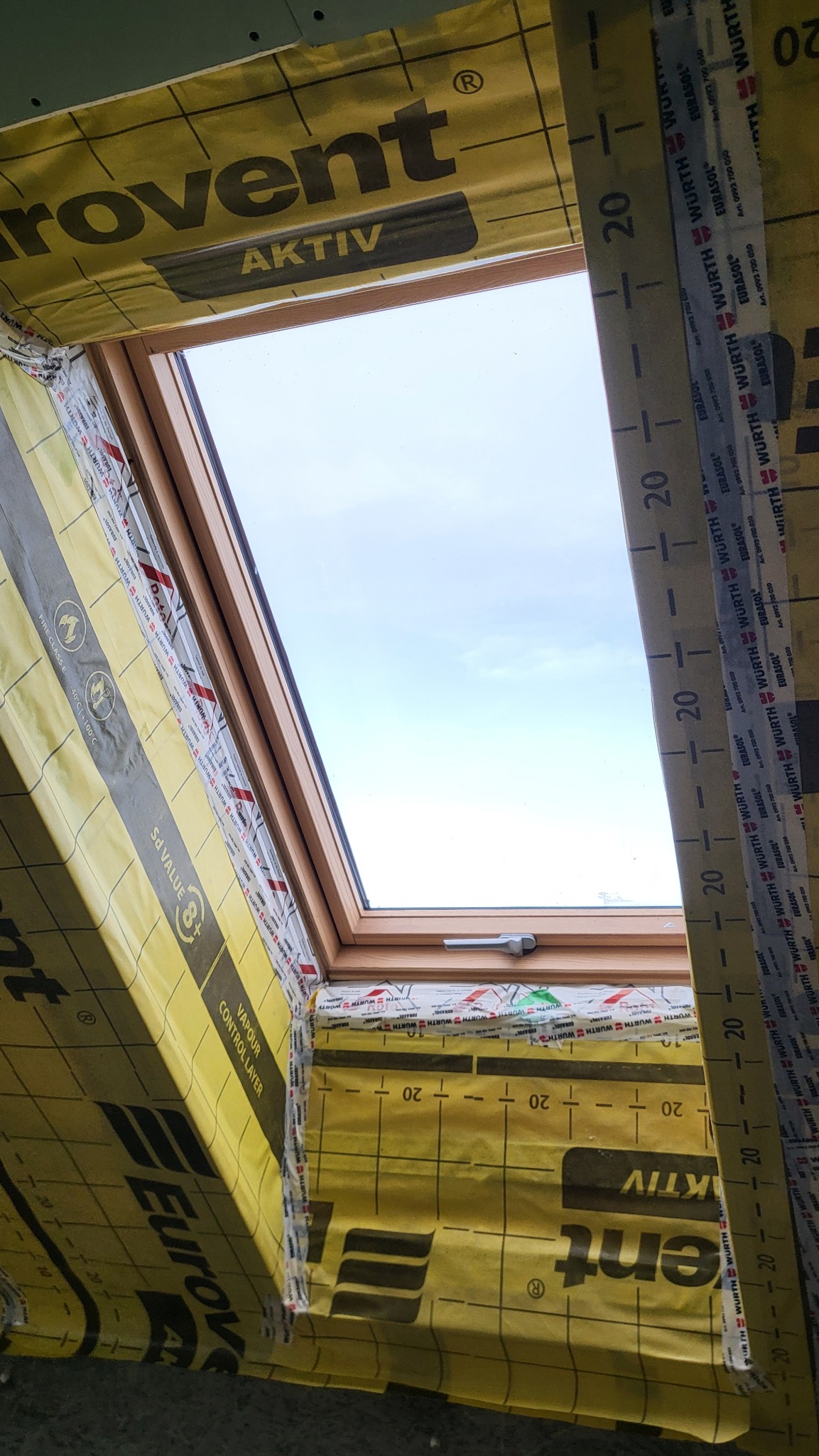 Montaż okna dachowego z folią paroizolacyjną Eurovent Aktiv, widoczne taśmy miernicze Wurth. Detal prac wykończeniowych na poddaszu.