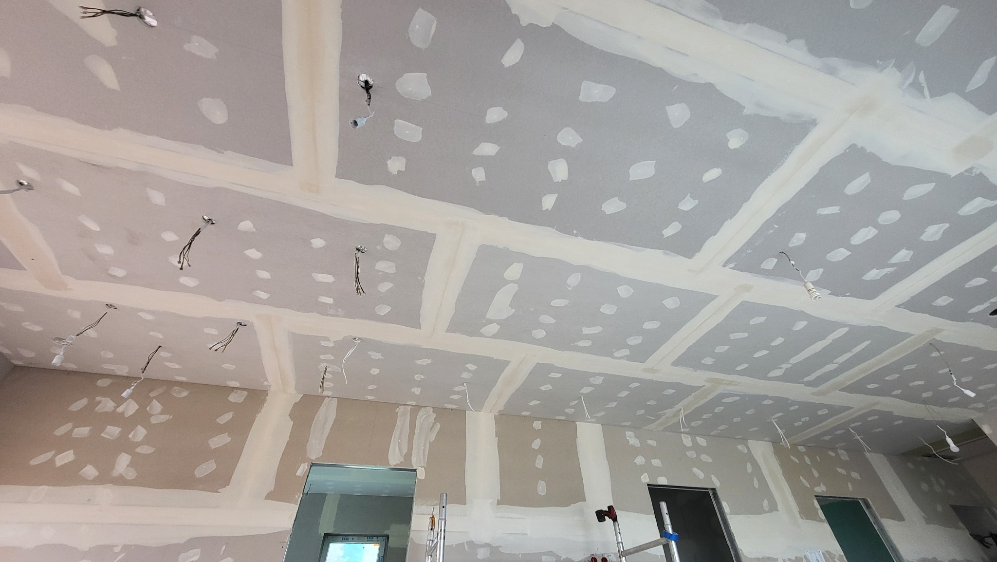 Sufit z płyt gipsowo-kartonowych po szpachlowaniu w Zielonej Górze, widoczne kable oświetleniowe i łączenia płyt. Prace wykończeniowe w trakcie realizacji.