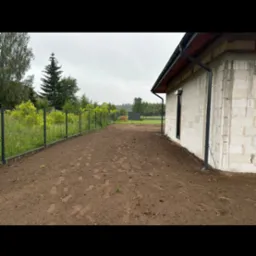 Przygotowany teren pod budowę domu z widocznymi fundamentami i ogrodzeniem z siatki.