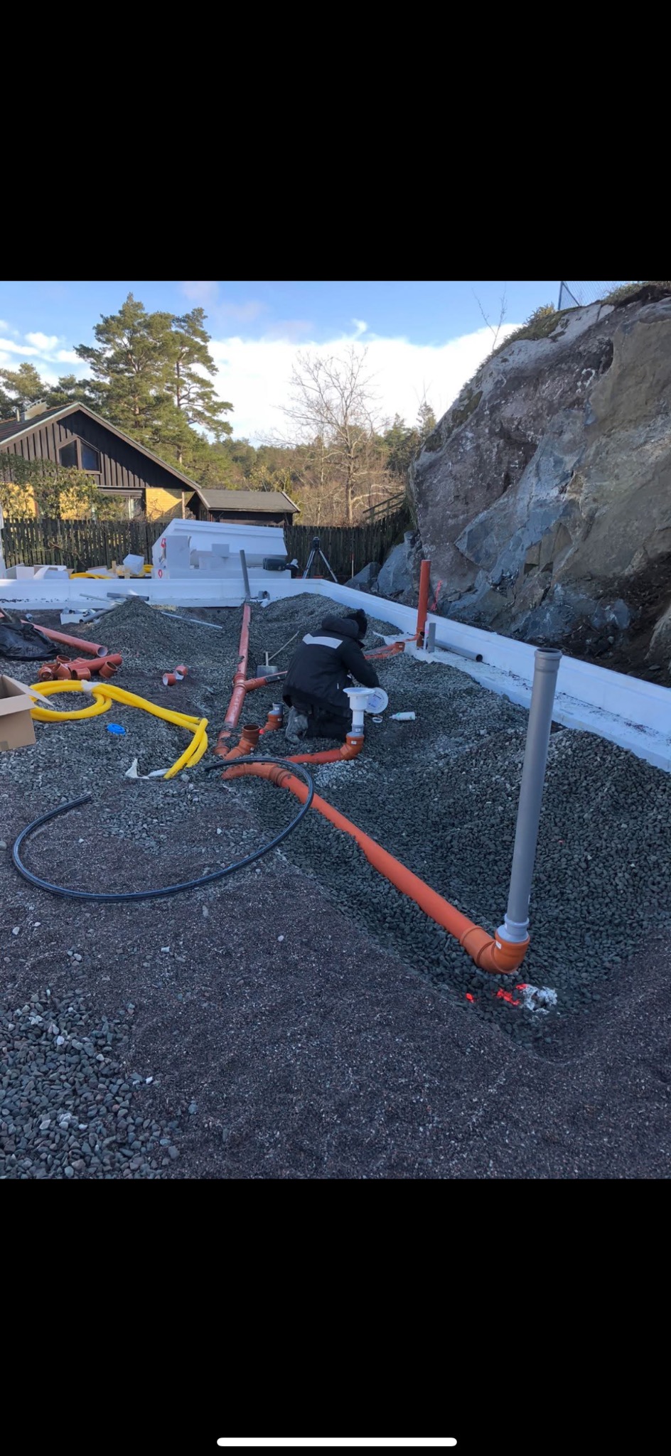 Instalacja rur kanalizacyjnych z tworzywa sztucznego w gruncie, widoczne fundamenty budynku i skaliste podłoże w tle.