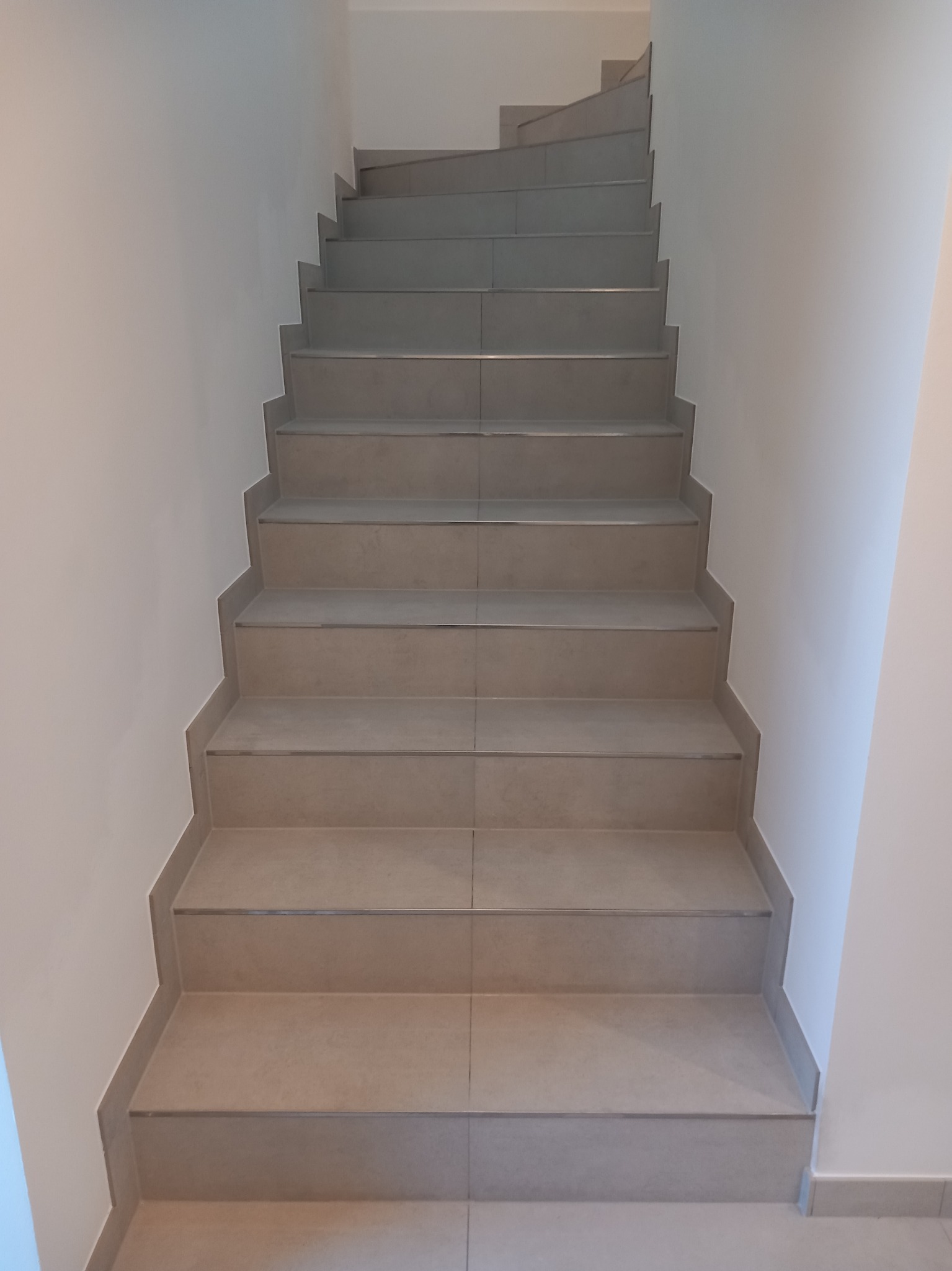 Schody wewnętrzne wykończone płytkami ceramicznymi w odcieniach beżu i szarości, widok z dołu, białe ściany.