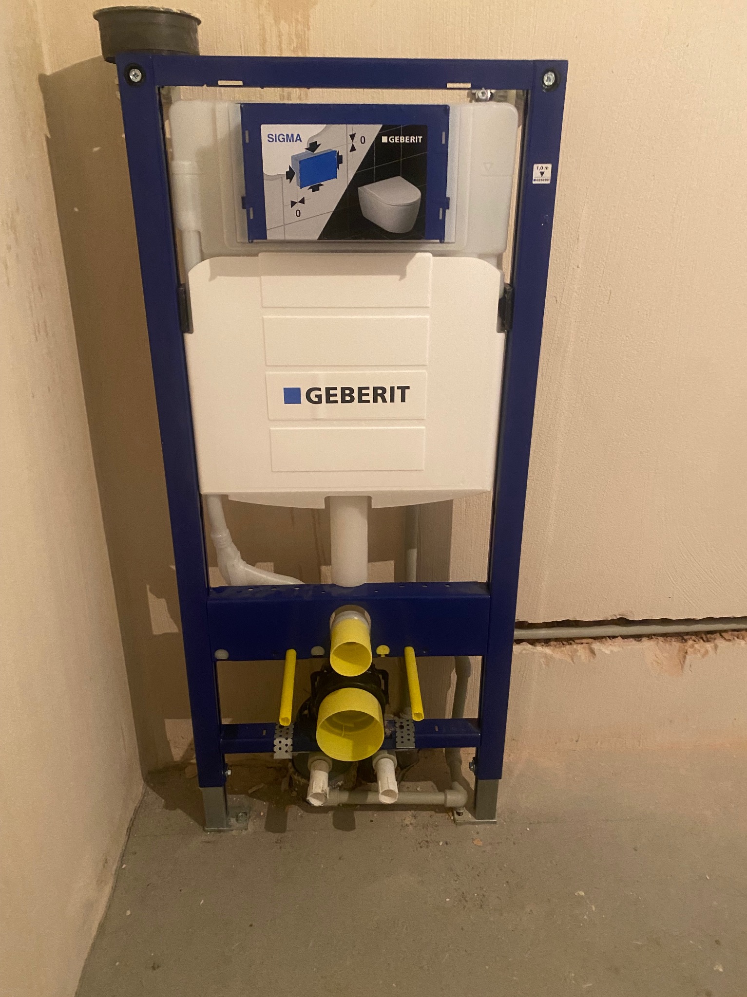 Stelaż podtynkowy Geberit Sigma z widocznymi elementami instalacji wodno-kanalizacyjnej, żółte rury odpływowe, surowa ściana w tle, etap montażu.