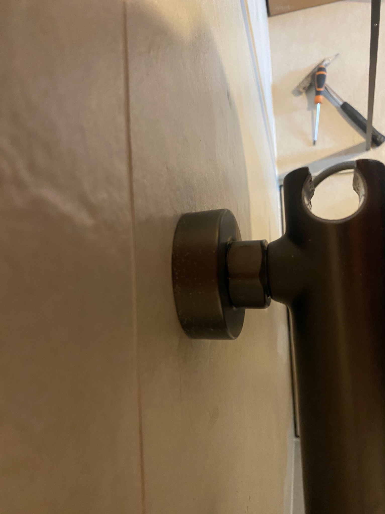 Zbliżenie na zamocowany, ciemny uchwyt prysznicowy na jasnej, wykafelkowanej ścianie, z widocznymi narzędziami w tle.