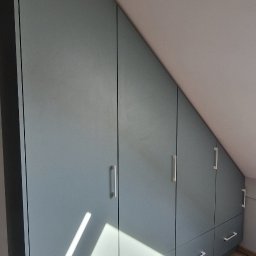 Meble & Tarasy - Niebieska zabudowa meblowa ze srebrnymi uchwytami, dopasowana do skosu poddasza, z widocznymi drzwiczkami i szufladami, na podłodze panele.