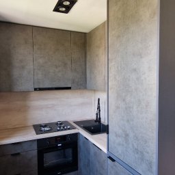 Meble & Tarasy - Nowoczesna kuchnia w odcieniach szarości z blatem imitującym drewno, czarnym zlewem i płytą indukcyjną, wykończona matowymi frontami i minimalistycznymi uchwytami.